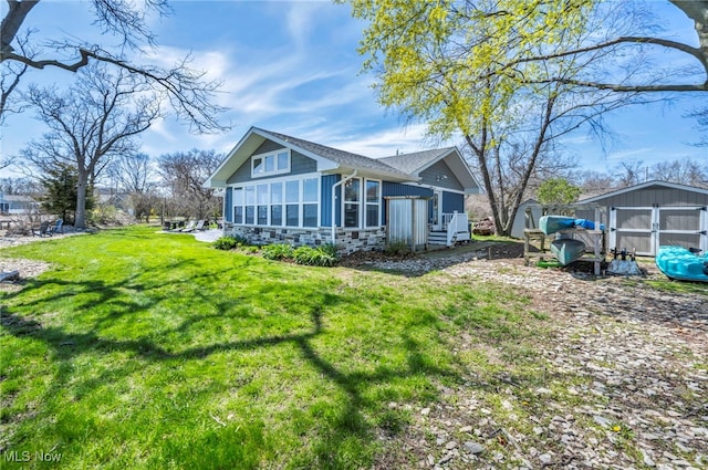 back of house with a lawn, a storage shed, a sunroom, an outdoor structure, and stone siding