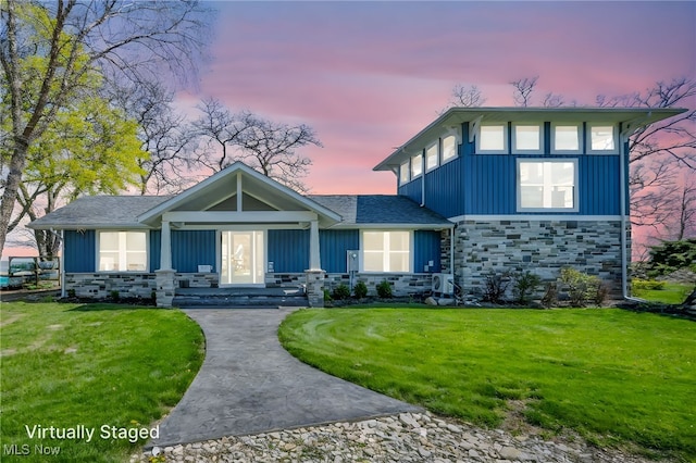 view of front facade with board and batten siding, a lawn, and stone siding
