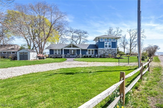 view of front of home featuring fence, a storage unit, a front lawn, stone siding, and an outdoor structure