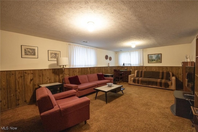 carpeted living area featuring wooden walls, a textured ceiling, visible vents, and wainscoting