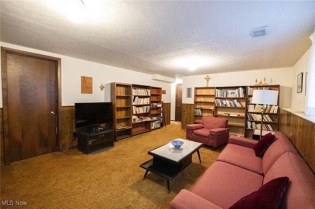 carpeted living area with wooden walls, wainscoting, a textured ceiling, and visible vents