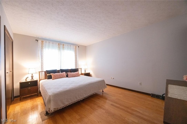 bedroom featuring baseboards, light wood finished floors, a textured ceiling, and visible vents