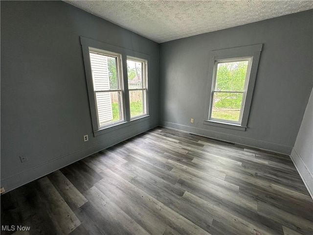 empty room with a healthy amount of sunlight, baseboards, a textured ceiling, and wood finished floors