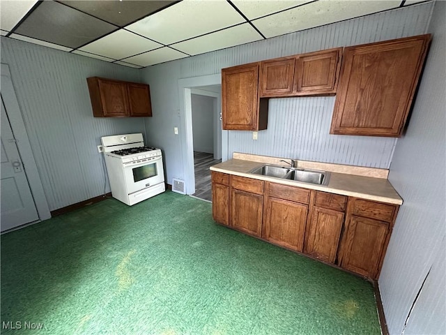 kitchen with brown cabinetry, a sink, a drop ceiling, and white gas range
