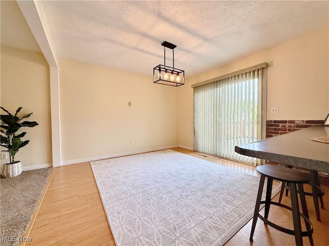 unfurnished dining area featuring baseboards, a textured ceiling, and wood finished floors