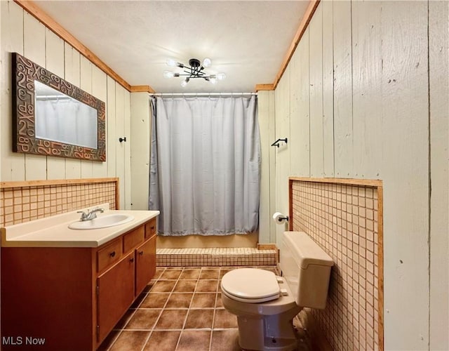 bathroom with tile patterned flooring, wood walls, ornamental molding, vanity, and toilet