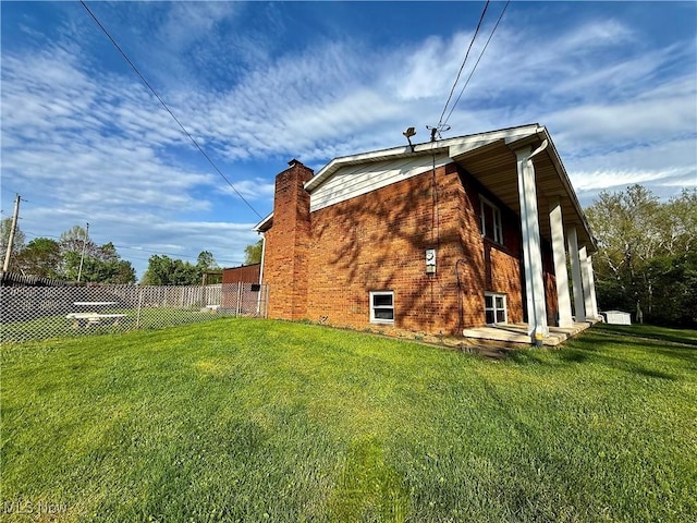 view of property exterior with a yard, brick siding, fence, and a chimney