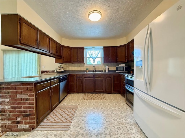 kitchen featuring decorative backsplash, dark countertops, a textured ceiling, a sink, and stainless steel appliances