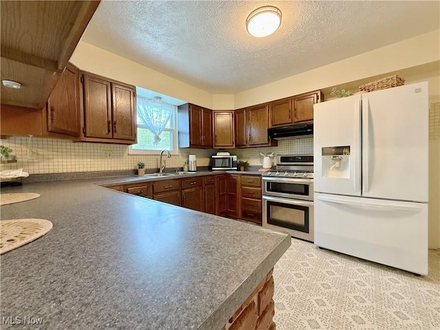 kitchen featuring stainless steel appliances, dark countertops, a sink, and tasteful backsplash