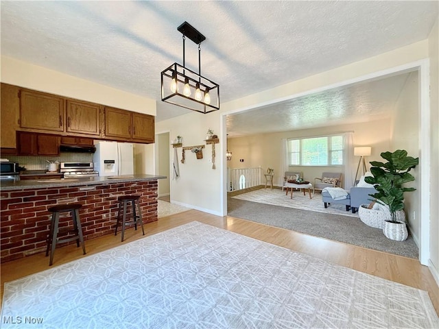 kitchen with dark countertops, open floor plan, light wood-style floors, white fridge with ice dispenser, and a breakfast bar
