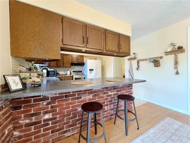 kitchen featuring stainless steel appliances, brown cabinetry, light wood finished floors, and a peninsula