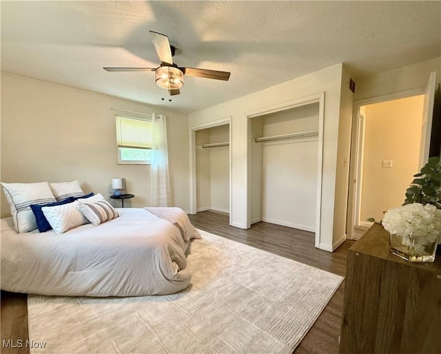 bedroom with a ceiling fan, baseboards, multiple closets, and dark wood finished floors