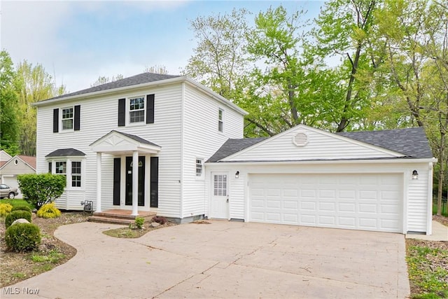 colonial house with roof with shingles, an attached garage, and driveway