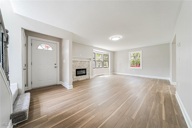 unfurnished living room with a stone fireplace, light wood finished floors, and baseboards
