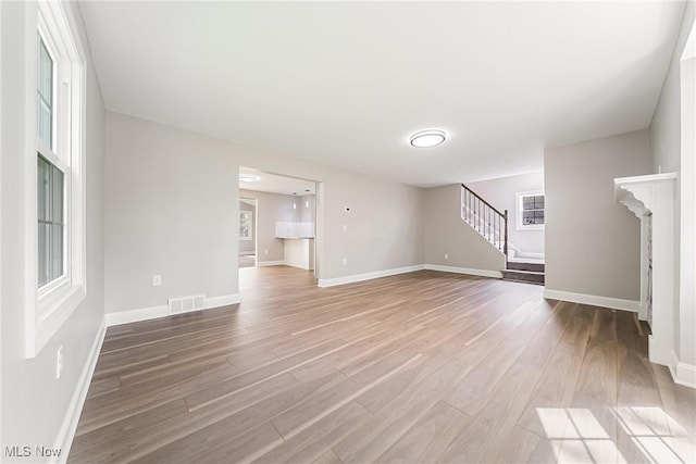 unfurnished living room featuring visible vents, baseboards, wood finished floors, and stairway