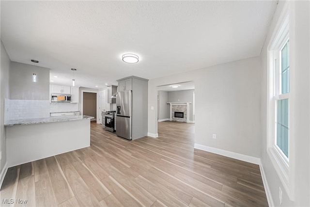unfurnished living room featuring light wood-style floors, baseboards, a wealth of natural light, and a stone fireplace