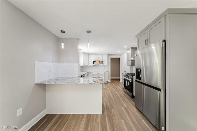 kitchen featuring pendant lighting, a peninsula, light wood-type flooring, tasteful backsplash, and appliances with stainless steel finishes