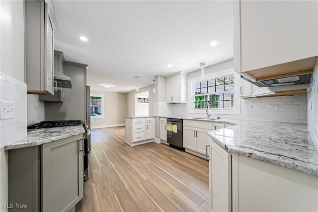 kitchen with a peninsula, light stone countertops, stainless steel range with gas stovetop, light wood finished floors, and dishwasher