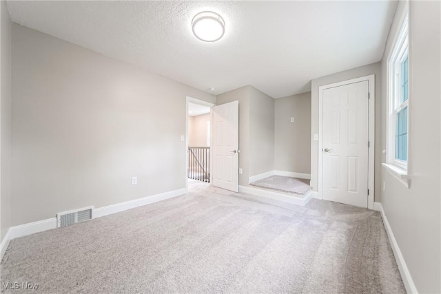 unfurnished bedroom featuring carpet floors, baseboards, a textured ceiling, and visible vents