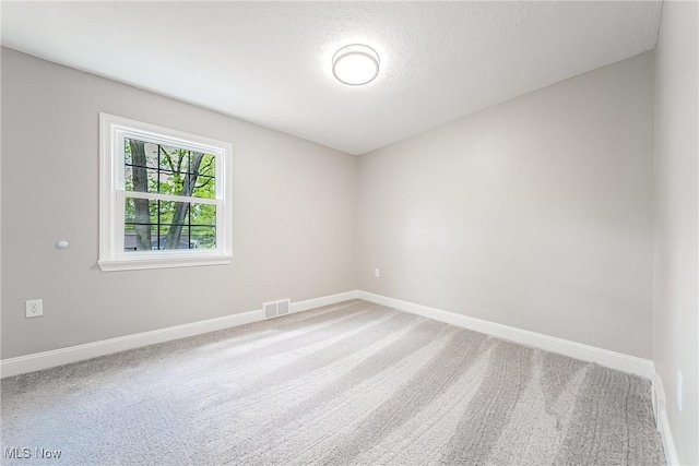 carpeted empty room featuring baseboards, a textured ceiling, and visible vents