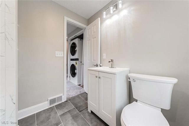 bathroom featuring stacked washer and dryer, vanity, toilet, baseboards, and visible vents