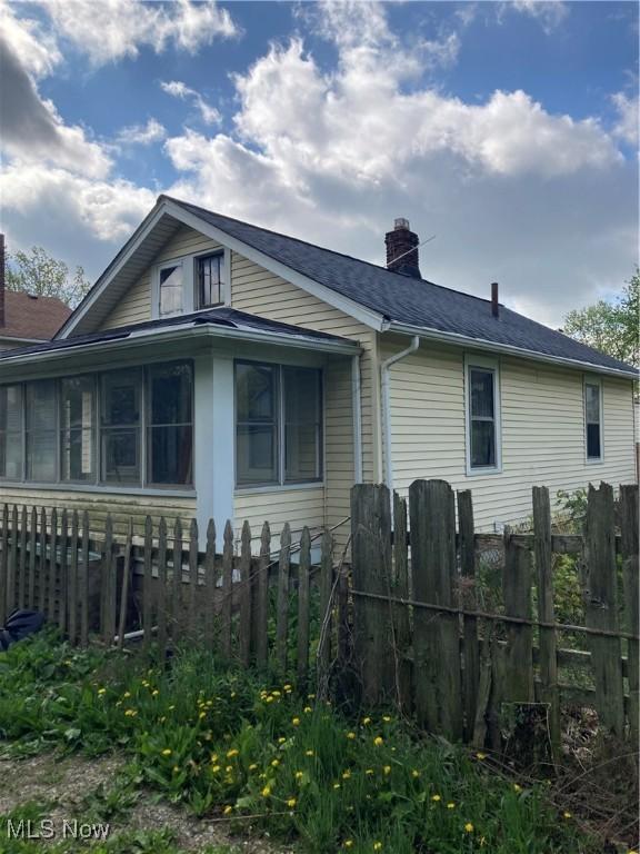 view of home's exterior with a sunroom, fence, and a chimney