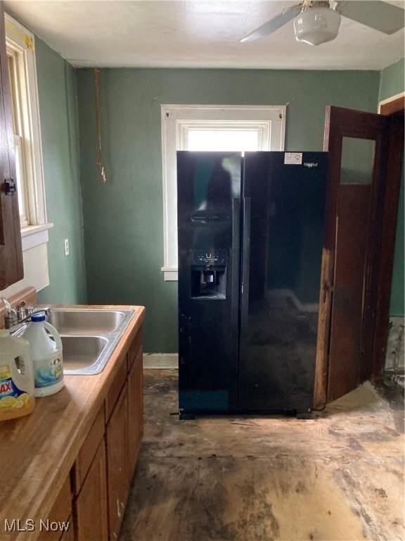 kitchen with ceiling fan, black refrigerator with ice dispenser, brown cabinetry, and a sink