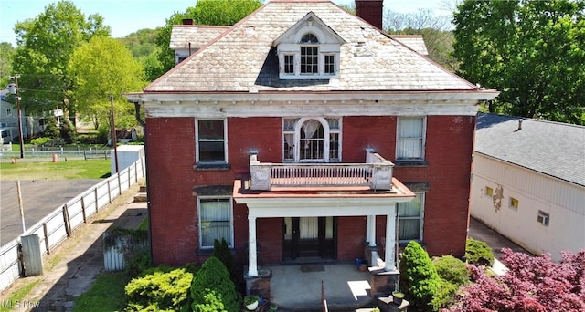 view of front of property featuring brick siding, a high end roof, a balcony, and a chimney