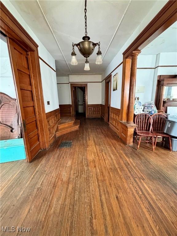 interior space featuring ornate columns, wood finished floors, and a wainscoted wall