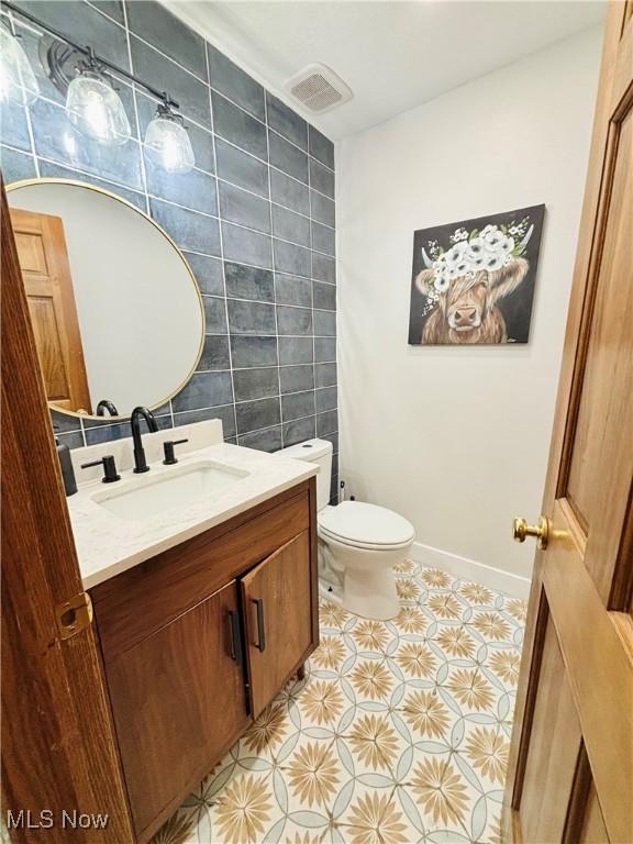 bathroom featuring vanity, tile patterned flooring, visible vents, toilet, and tile walls
