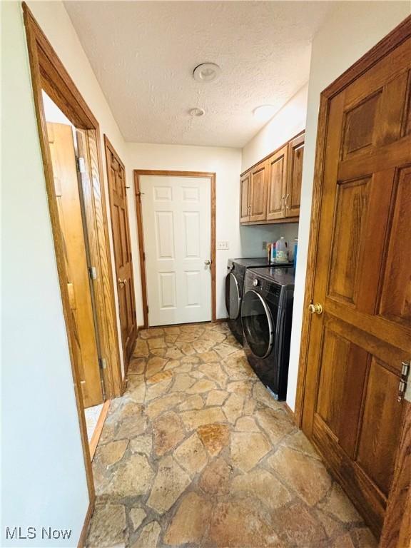 washroom featuring a textured ceiling, stone flooring, cabinet space, and washer and dryer