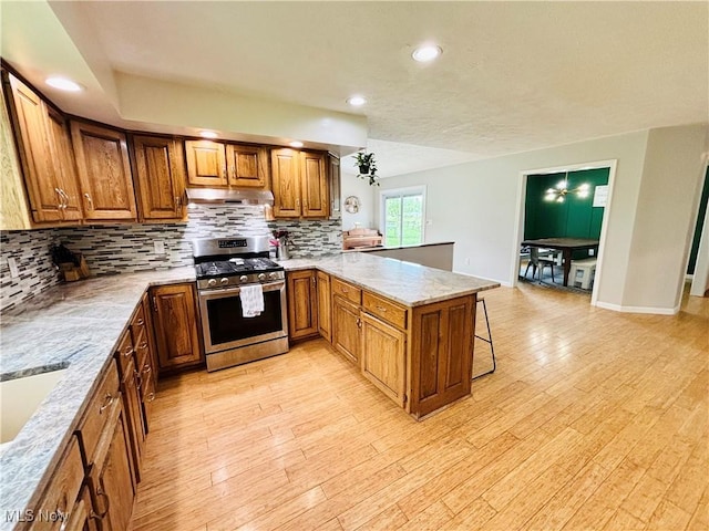 kitchen with a breakfast bar, stainless steel gas range oven, brown cabinetry, a peninsula, and tasteful backsplash