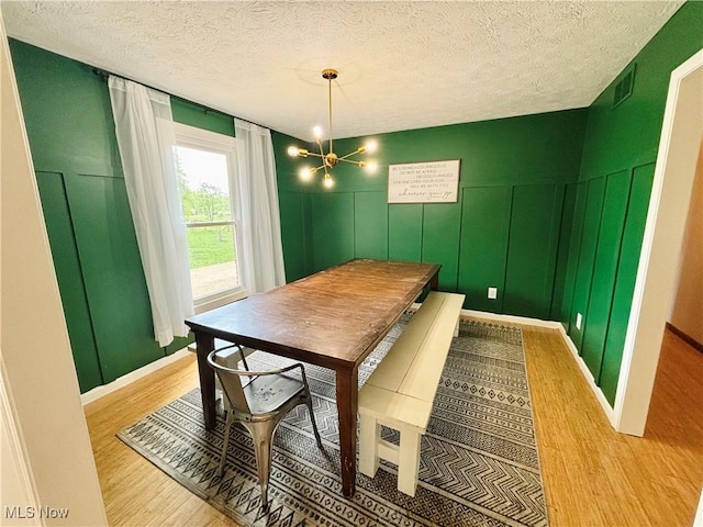 dining area featuring visible vents, a decorative wall, light wood-type flooring, a textured ceiling, and a chandelier