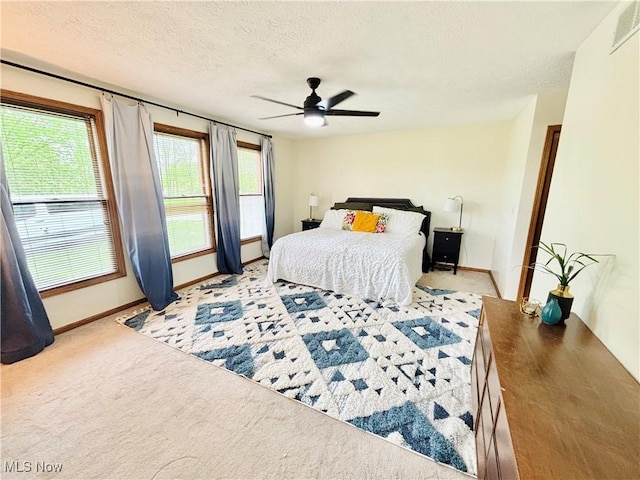 bedroom with a ceiling fan, a textured ceiling, visible vents, light colored carpet, and baseboards