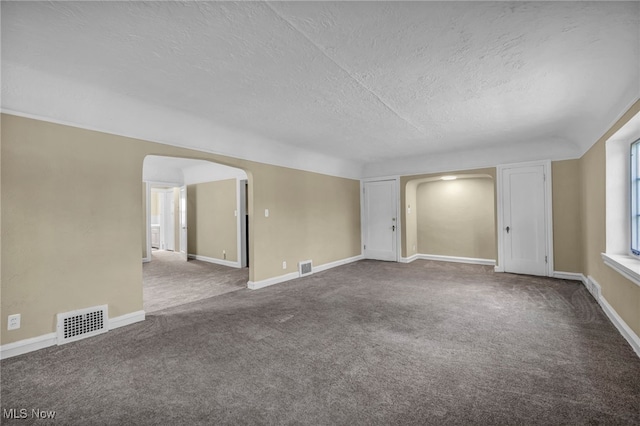 unfurnished room with carpet floors, arched walkways, a textured ceiling, and visible vents