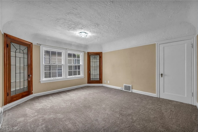 empty room featuring carpet flooring, a textured ceiling, baseboards, and visible vents