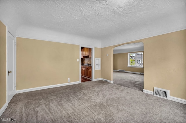 unfurnished room with arched walkways, a textured ceiling, dark colored carpet, baseboards, and visible vents