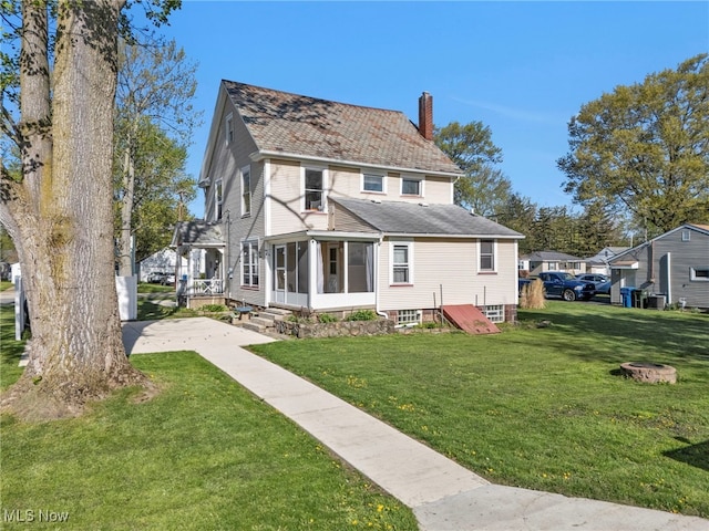 rear view of property featuring a sunroom, a yard, and a chimney