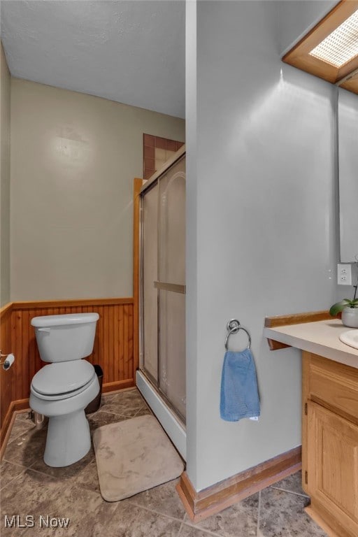 bathroom with vanity, wood walls, toilet, a wainscoted wall, and a shower stall
