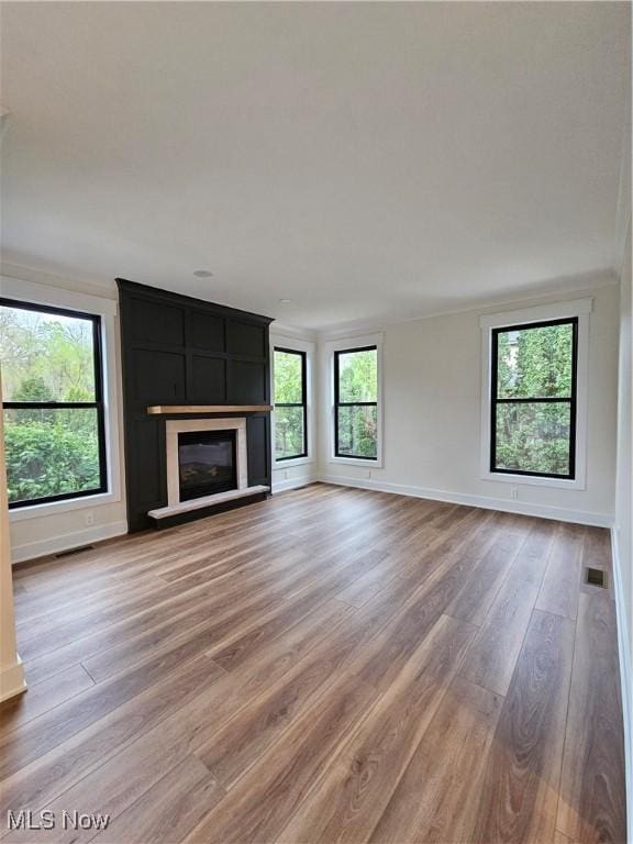 unfurnished living room featuring light wood-style floors, baseboards, a wealth of natural light, and visible vents