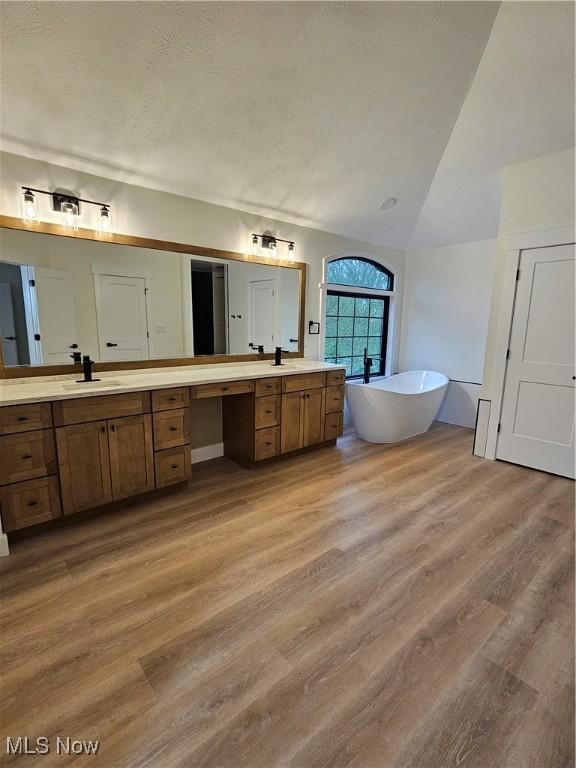 full bathroom with a sink, two vanities, wood finished floors, lofted ceiling, and a soaking tub