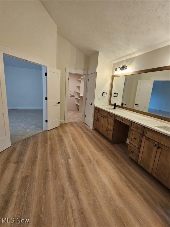 bathroom featuring a sink, double vanity, baseboards, wood finished floors, and vaulted ceiling
