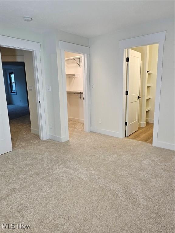 unfurnished bedroom with a closet, a walk in closet, baseboards, and carpet flooring