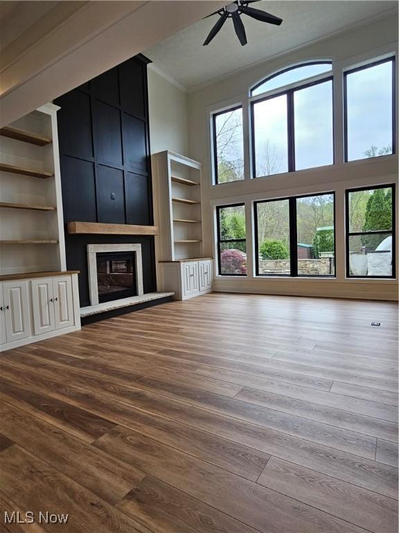 unfurnished living room with a ceiling fan, a towering ceiling, crown molding, a large fireplace, and wood finished floors