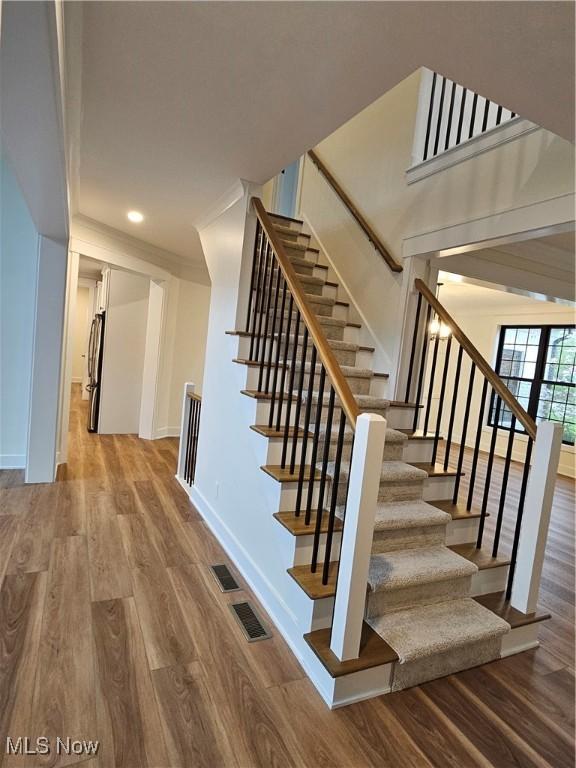 stairs with baseboards, ornamental molding, wood finished floors, and visible vents