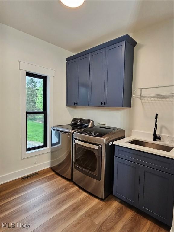washroom featuring visible vents, cabinet space, a sink, light wood-style floors, and washer and dryer