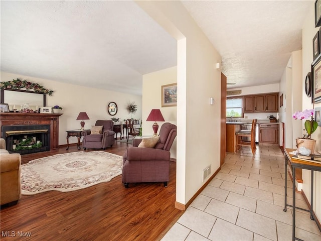 living room with a fireplace, a textured ceiling, light wood-style flooring, baseboards, and visible vents