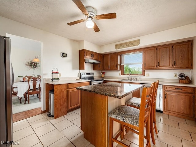 kitchen with light tile patterned flooring, brown cabinetry, appliances with stainless steel finishes, and a breakfast bar