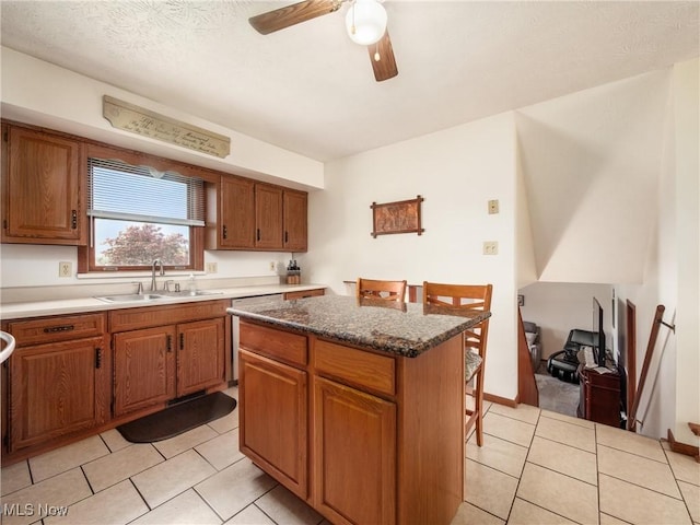 kitchen with brown cabinets, a sink, a center island, a ceiling fan, and light tile patterned floors