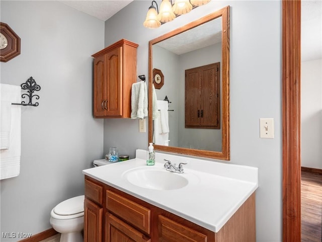 bathroom featuring vanity, wood finished floors, toilet, baseboards, and a notable chandelier